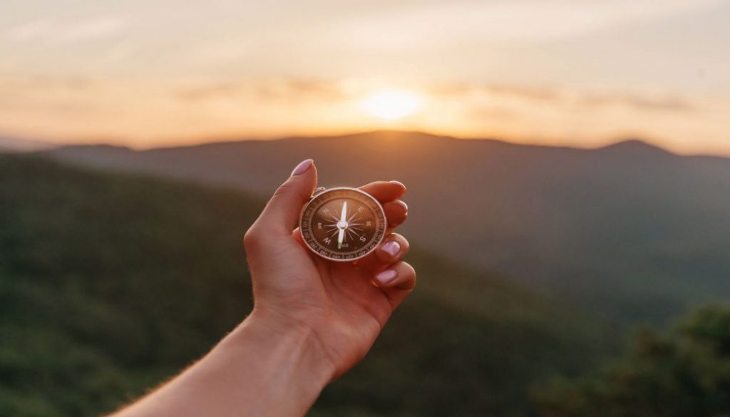 Female hand with compass in summer mountains at sunrise, pov. cum-sa-ti-descoperi-scopul
