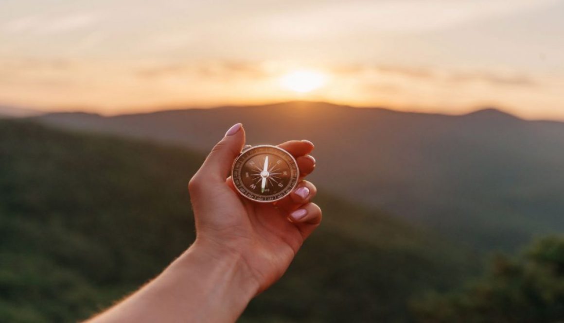 Female hand with compass in summer mountains at sunrise, pov. cum-sa-ti-descoperi-scopul